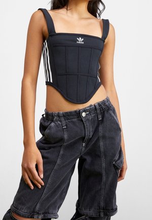 Vrouw draagt een zwarte Adidas korsettop met witte strepen en losse zwarte denimshorts met opgerolde zomen.