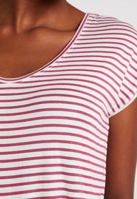 Červeno-bílý pruhovaný top s krátkým rukávem a výstřihem do V. Měkká bavlněná látka s rovnoměrně rozloženými horizontálními pruhy a uvolněným střihem.