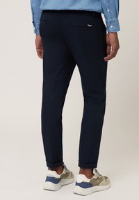 Tmavomodré nohavice vyrobené z ľahkého materiálu, so slim fit strihom, bočnými vreckami a zvinutými nohavicami, skombinované s teniskami.