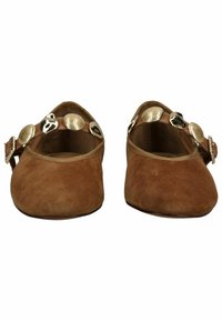 Ruskeat mokkanahkaiset matalakorkoiset kengät, joissa kullanvärisiä ja mustia koristekyniä remmeissä jalkapöydän kohdalla, nähtynä edestä.