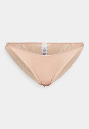 Bas de bikini beige en tissu microfibre lisse, avec des accents en dentelle florale sur les côtés. Étiquette visible à l'intérieur avec les informations de marque.