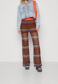 Klippt denimjacka över en orange topp, parat med utsvängda, flerfärgade stickade byxor med horisontella ränder och chunky blå plattformsskor.