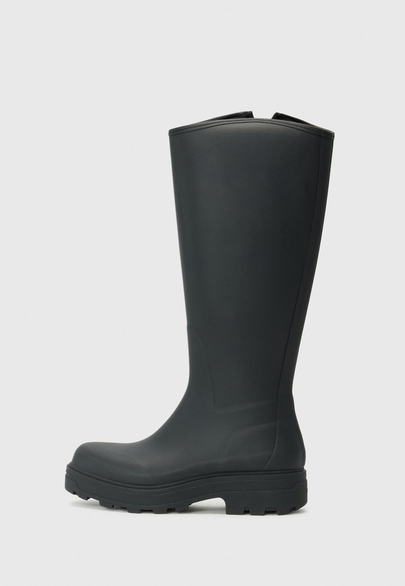 Botas de borracha pretas até ao joelho com biqueira redonda e sola texturizada para aderência. Acabamento suave com um ligeiro brilho e detalhes de costura nas laterais.