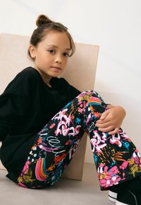 Svart långärmad skjorta i kombination med färgglada, mönstrade utsvängda byxor med graffiti-liknande motiv i rosa, blå och gula nyanser.