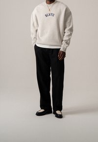 Sudadera gris claro con "BLKVIS" en color marino, combinada con pantalones negros y mocasines negros con un detalle frontal de malla beige.