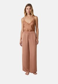 Lichtbruin satijnen cami-top met kantafwerking, gecombineerd met losse lichtbruine stoffen broek. Eenvoudig ontwerp met elastische tailleband en trekkoord.