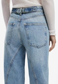 Jean en denim bleu clair à taille haute, doté de deux poches arrière, de coutures visibles et d'une texture légèrement délavée.