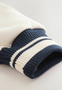 Strikket sweatshirtmanchet i marineblå og creme, med ribbet tekstur og to creme striber på den marineblå bånd. Glat stof over manchetten.