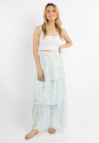 Fehér bordázott crop top egy világos kék, laza, réteges maxi szoknyával, amelynek batikolt mintázata van. Az öltözetet lapos szandálok egészítik ki.