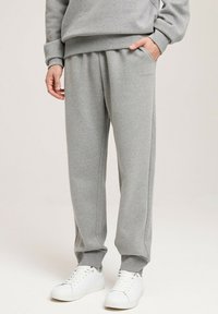 Szare dresy wykonane z miękkiego materiału, z elastycznym pasem i ściągaczami na kostkach. Połączone z białymi sneakerami dla swobodnego wyglądu.