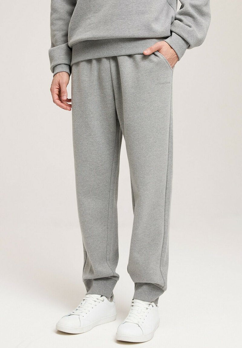 Szare dresy wykonane z miękkiego materiału, z elastycznym pasem i ściągaczami na kostkach. Połączone z białymi sneakerami dla swobodnego wyglądu.