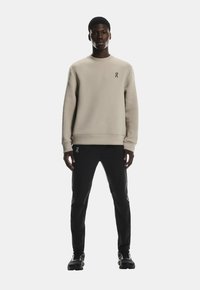 Sweatshirt bej deschis, cu guler rotund, textură moale și un logo mic. Combinat cu pantaloni slim-fit negri și pantofi sport negri.