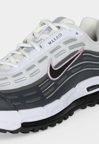 Λευκό και γκρι αθλητικό παπούτσι Nike Max Air με μαύρο και ροζ σήμα, πλέγμα επάνω μέρος και μαλακή σόλα με ορατή μονάδα Max Air.