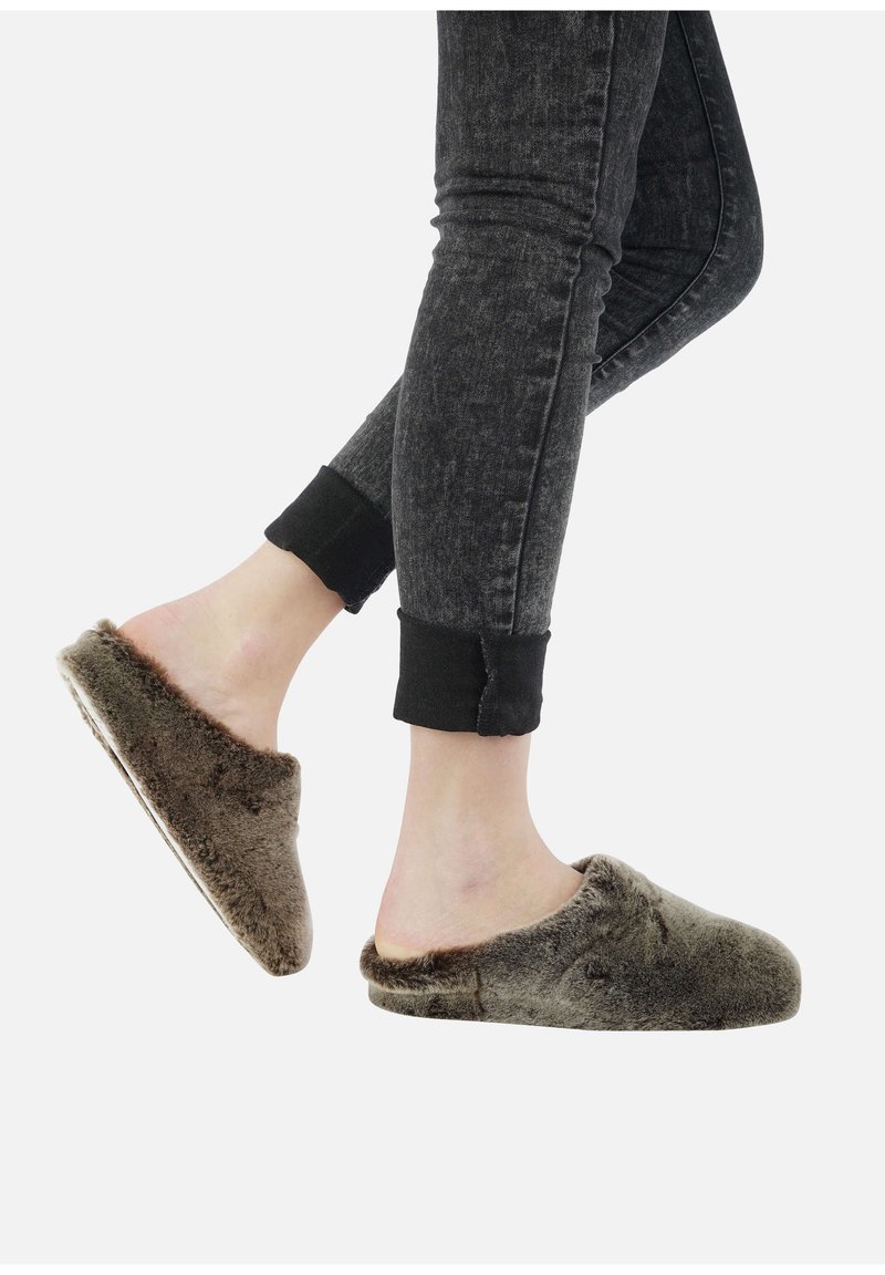 Chaussons marron en peluche avec une texture douce et un design à l'arrière ouvert. Associés à un pantalon en denim sombre et retroussé.