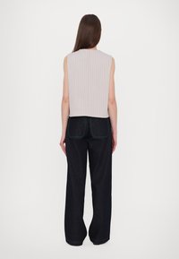 Haut sans manches gris clair avec une texture à côtes verticales, associé à un pantalon large en denim foncé avec des surpiqûres vertes contrastantes et des détails de poches.