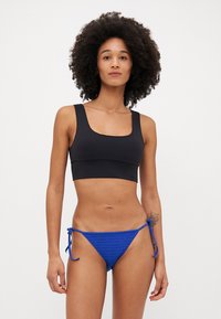 Black athletic crop top with square neckline paired with blue bikini bottom featuring a textured pattern and adjustable tie sides.