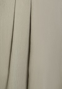 Close-up of light beige fabric showing detailed diagonal weave texture and sharp, vertical folds.