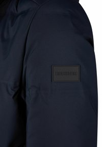 Marineblauwe gewatteerde jas met een gladde textuur en een zwart rubberen logopatch met "HECHTER" op de linker schouder.