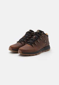 Botas de senderismo de cuero marrón con acentos negros, que cuentan con una superficie texturizada, un sistema de lazada reforzado y una suela de goma resistente.