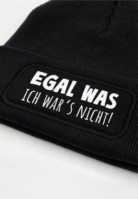 Black knitted beanie featuring a rectangular patch with white lettering that reads "EGAL WAS ICH WAR'S NICHT!" and subtle ribbed texture.