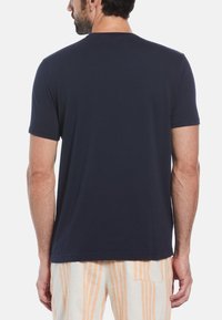 Navy blue cotton T-shirt with short sleeves, crew neck, and a plain design; worn with striped beige and orange pants.