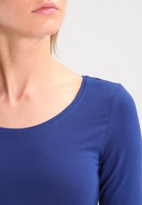 Długi rękaw, okrągły dekolt w jednolitym kobaltowym kolorze, wykonany z gładkiego, rozciągliwego materiału, z dopasowanym krojem i subtelnymi detalami w szwach.