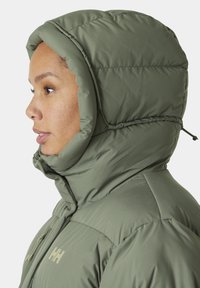 Chaqueta acolchada verde con una capucha alta y suave. Presenta un textura acolchada y un cierre frontal de cremallera. Logo visible en el pecho.