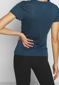 Blå kortärmad t-shirt i mjukt material, figurnära design, rund halsringning och slät textur. Buren tillsammans med svarta leggings.
