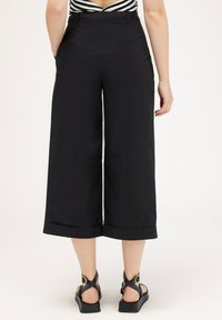 Culottes noirs à jambe large, avec une texture lisse, taille mi-haute et ourlets retroussés. Associés à des sandales noires à lanières.