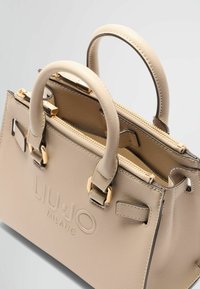 Sac à main structuré beige en matériau synthétique texturé, doté de doubles poignées et d'accents en métal doré. Comprend un compartiment zippé.