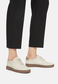 Beżowe codzienne trampki wykonane z gładkiego materiału, z zapięciem na sznurówki, jasnobrązowymi akcentami i teksturowanymi gumowymi podeszwami.