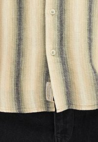 Gestreept shirt in beige en zwart, met knoopsluiting en gestructureerde stof. Voorzien van een waslabel aan de zoom.