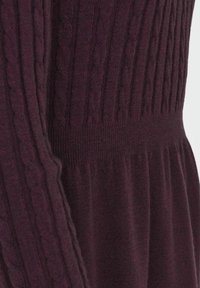 Gros plan sur un tissu tricoté violet foncé avec des motifs torsadés et côtelés sur la manche et le corsage.