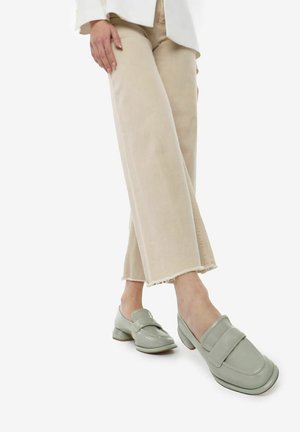 Mocassini in vernice verde chiaro con punta rotonda, caratterizzati da una striscia decorativa. Indossati con pantaloni beige larghi.