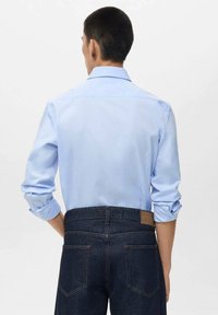 Light blue long-sleeve shirt with a folded collar, rolled cuffs, paired with dark denim jeans, featuring a brown leather patch on the waistband.