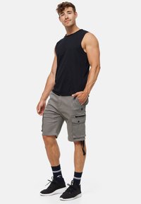 Shorts cargo gris avec plusieurs poches, un cordon de serrage et une coupe décontractée. Associés à un t-shirt sans manches noir et des baskets noires.