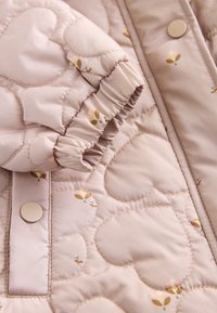 Manche de veste matelassée rose clair avec coutures en forme de cœur, petit imprimé floral, boutons-pression et poignet élastique.
