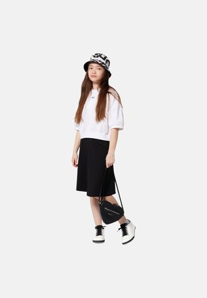 Witte cropped sweatshirt, zwarte rok, zwarte bucket hat met witte patroon, zwarte crossbody tas en zwart-witte sneakers.