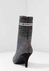 Bottines à talons en tricot texturé noir et gris, présentant un tige côtelée et deux rayures blanches horizontales autour du bord supérieur.