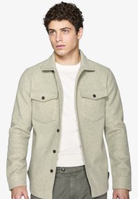 Lys grøn flannel skjortejakke med to brystlommer, knaplukning, blød tekstur og klassisk krave. Bæres over en hvid sweater.