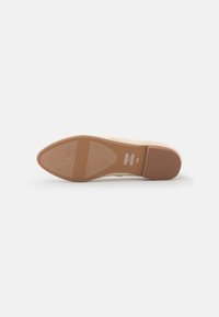 Beige platt sko liggande på sidan som visar den texturerade bruna sulan med TOMS-logotypen och storleken W6.