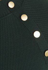 Dunkelgrüner, gerippter Stoff mit einem schrägen Design, verziert mit großen goldenen Knöpfen entlang der Schulterlinie.