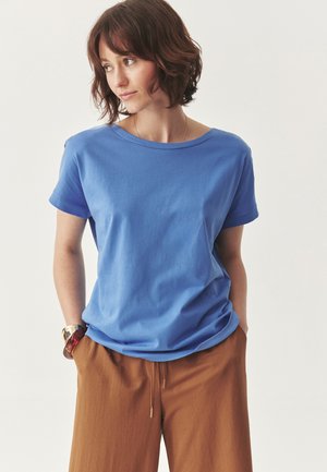 T-shirt in cotone blu con maniche corte e scollatura rotonda, abbinata a pantaloni beige a gamba larga. Design minimalista senza motivi visibili.