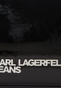 Fekete fényes anyag, melyen domború ezüst szöveg olvasható: "KARL LAGERFELD JEANS", sima, tükröződő felülettel és modern dizájnnal.