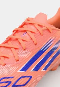 Scarpa da calcio arancione brillante con materiale testurizzato, presenta strisce diagonali blu, lacci coordinati e un design elegante e aerodinamico.
