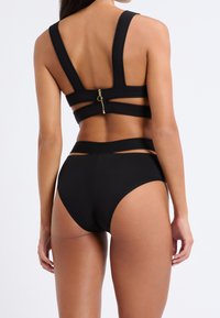 Haut de bikini noir à côtes avec des bretelles larges et une fermeture éclair. Bas noir taille haute au design épuré et avec une couverture minimale sur les côtés.