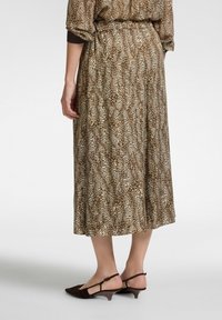 Abito midi con stampa leopardata, caratterizzato da una palette di colori marrone e beige, in tessuto leggero e con una silhouette fluida. Abbinato a tacchi slingback marroni.