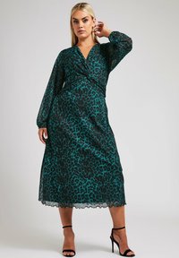Teele und schwarzes Leopardenmuster-Kleid mit Wickeldesign, langen transparenten Ärmeln und gewelltem Saum. Tragen mit schwarzen Riemchen-Heels.