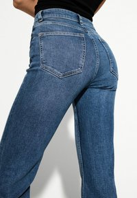 Blaue Jeans aus Denim mit einer schmalen Taille und ausladenden Beinen. Verfügt über zwei Gesäßtaschen und eine glatte, robuste Textur.