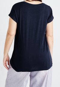 Navy blue short-sleeve top with a relaxed fit and rounded neckline, featuring a smooth texture and slightly curved hem.